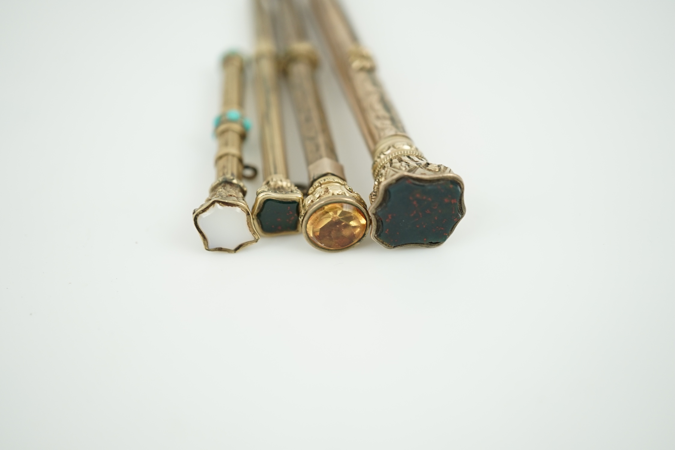 Four assorted late 19th/early 20th century yellow metal overlaid and gem set propelling pencils, largest set with bloodstone with pen and pencil, 97mm.